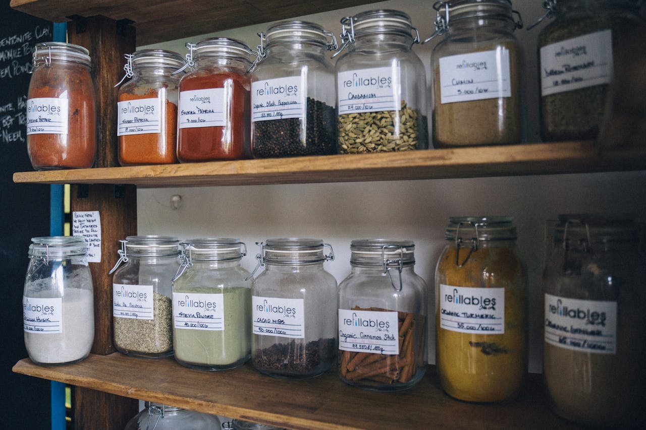 Glass jars filled with spices and labels on a wooden shelf for eco-friendly storage.