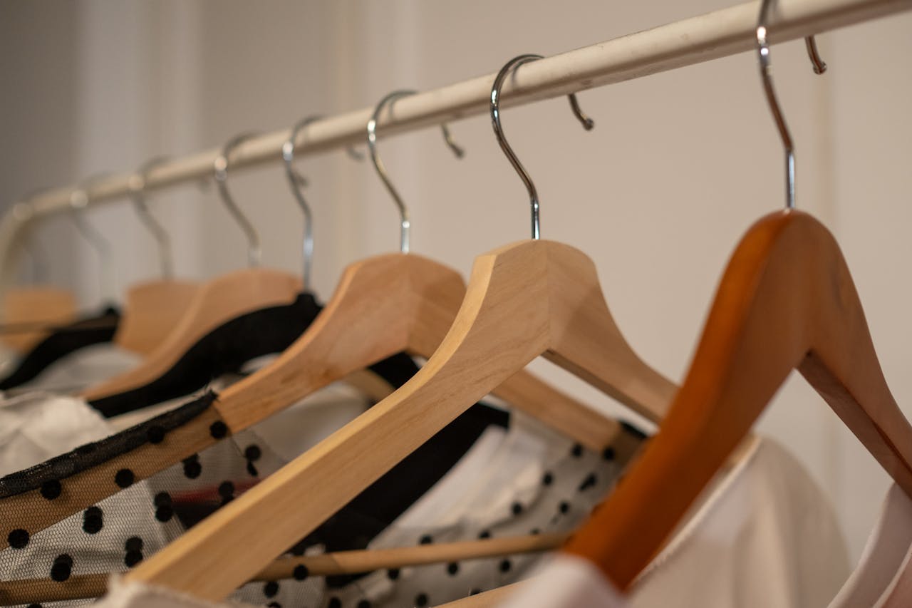 Close-up of wooden clothes hangers with assorted clothing indoors.